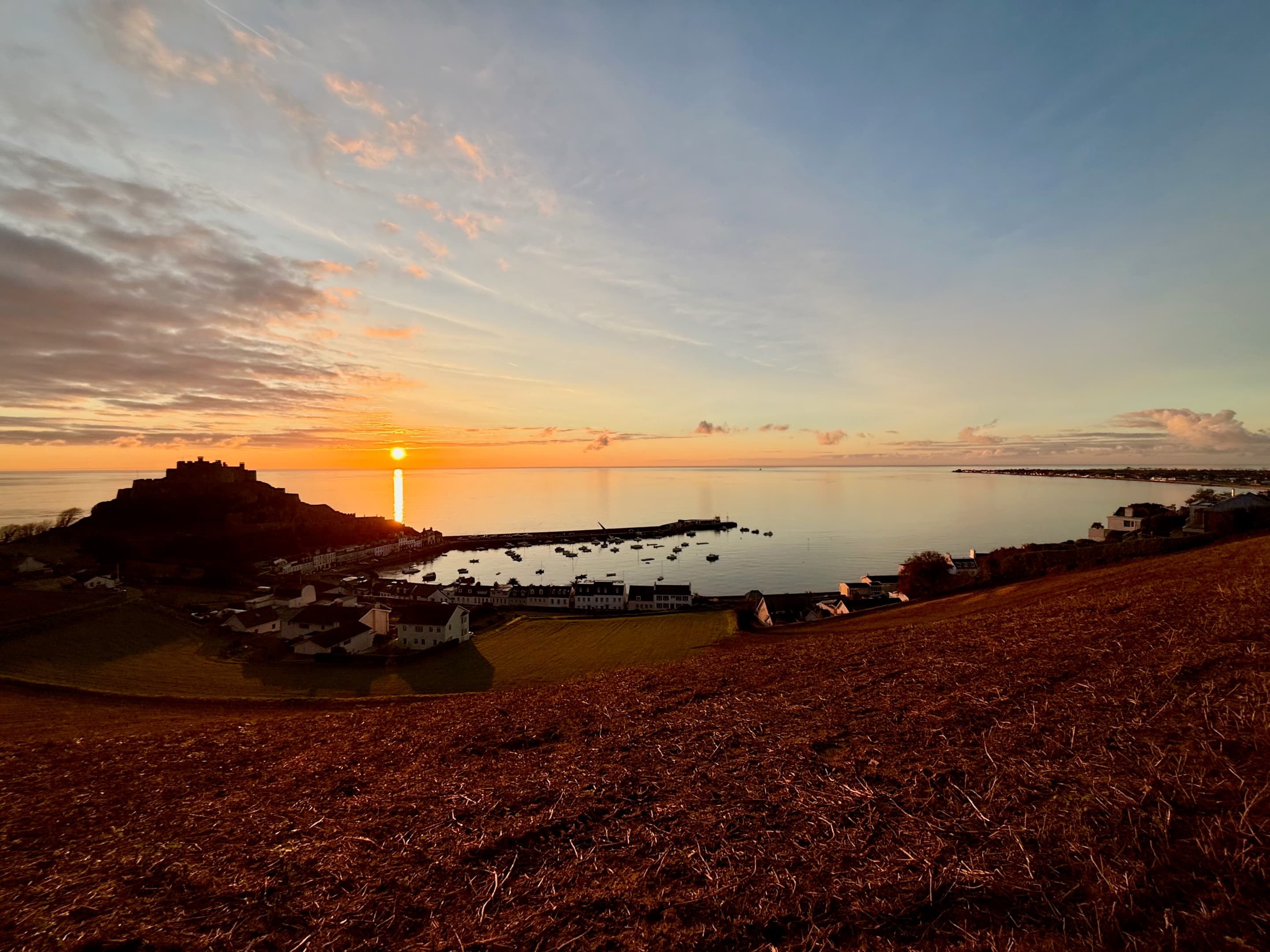 Sunrise over a coastal harbour with a castle in silhouette